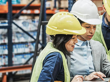 Team members look at a laptop screen inside a warehouse Team members look at a laptop screen inside a warehouse